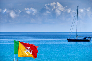 Fototapeta premium cruising sailboat moored on the clear sea with the flag of Sicily blowing in the wind