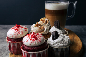 Variety of delicious cupcakes with a cup of coffee served on a wood tablet. Dark background of red...