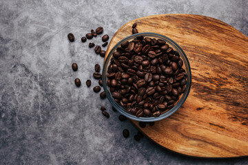 Coffee beans in a transparent bowl over a wood tablet with copy space. Dark background of coffee beans.