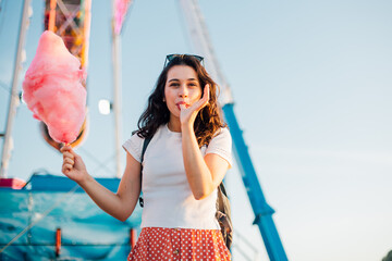 Funny young woman eating cotton candy at fairground