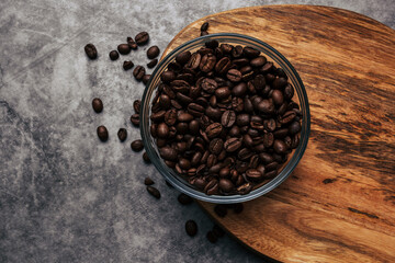 Coffee beans in a transparent bowl over a wood tablet with copy space. Dark background of coffee beans.