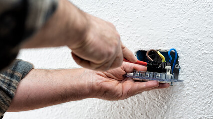 Electrician worker with screwdriver fixes electrical cables in the terminals of the socket of an electrical system. Construction industry.