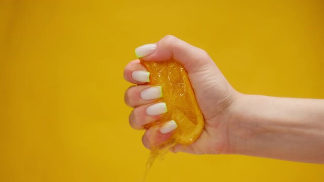 Close-up of squeezing orange juice with splashes by female hand on orange background, making citrus fruit drink, shooting of cocktail of orange, lemonade from sliced fruits. 