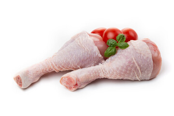 Raw chicken legs with skin decorated with tomatoes and basil on a white background.