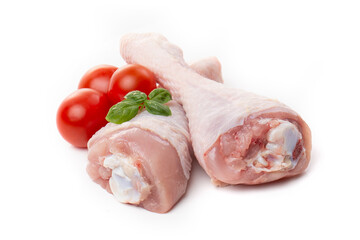 Raw chicken legs with skin decorated with tomatoes and basil on a white background.