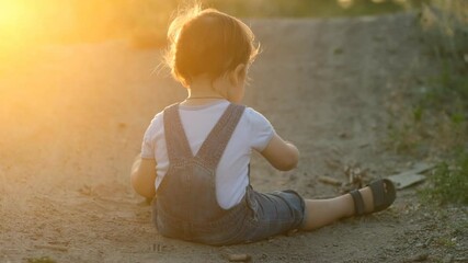 The kid is exploring the world around him. Happy childhood. Evening walk with the baby. The kid meets and studies the sand and earth in the park.