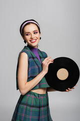 happy young woman in headband holding retro vinyl disc isolated on grey.