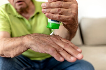 Close up shot of a senior man applying hand cream in bedroom. Mature Caucasian mans hands squeezing tube and applying hand lotion skin care product. Male hands close up, dry skin, skin care concept.