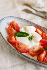 Traditional Italian salad with Burrata cheese, tomatoes and fresh basil. Mozzarella burrata salad with basil leaves and tomatoes on plate on beige linen tablecloth