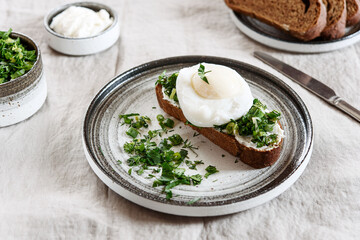 Healthy Breakfast with Poached Egg on toast with cream cheese and chopped mix of green onions, dill and parsley on greige linen tablecloth