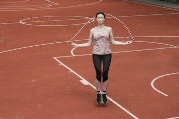 Young woman skipping jump rope on a sport field
