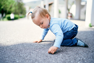 Little girl with a ponytail sits on her knees on the road in the park
