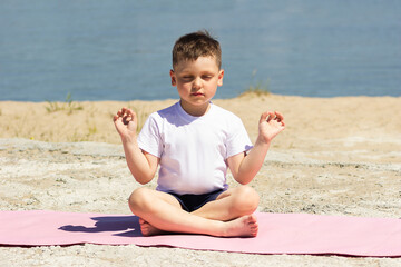 A little caucasian boy meditates holding fingers in yoga sign with his eyes closed sitting on a mat...