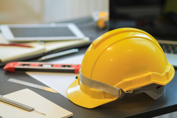 The engineering team's equipment and documents on the desks in the office, as well as the yellow helmets prepared to be worn when entering the site for safety on the desks.