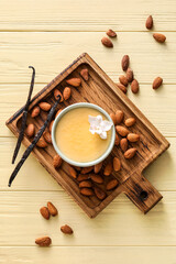 Board with tasty vanilla pudding in ramekin and almond on color wooden background