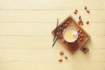 Board with tasty vanilla pudding in ramekin and almond on color wooden background
