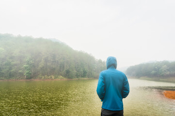 Rear view of young man in hoodie jacket surrounded by mist standing beside the lake and looking to far away , inspiration , motivation , freedom , hope and dream concept