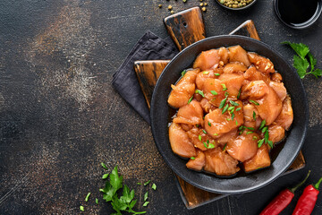 Raw chicken meat marinated in teriyaki soy sauce, onions and pepper in a black plate on a dark slate, stone or concrete background. Top view with copy space.