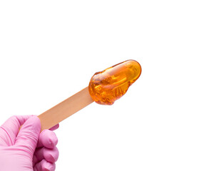 A female hand in a pink glove holds a wooden stick with yellow sugar paste or wax for depilation on a white background. Epilation, depilation, hair removal, beauty. Isolated.Copy space.Place for text - obrazy, fototapety, plakaty