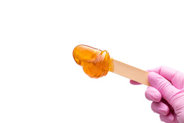 A female hand in a pink glove holds a wooden stick with yellow sugar paste or wax for depilation on a white background. Epilation, depilation, hair removal, beauty. Isolated.Copy space.Place for text - obrazy, fototapety, plakaty