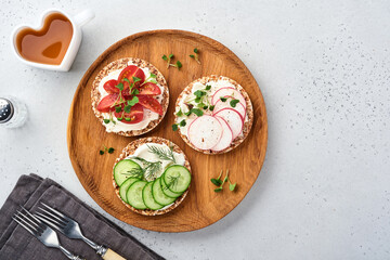 Three crispy buckwheat bread gluten free with cream cheese, radish, tomato, cucumber and microgreen for healthy breakfast on parchment paper on stone background . Concept vegan and healthy eating.