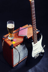 Combo amplifier for guitar with black guitar, glass of beer and notepad on black background.