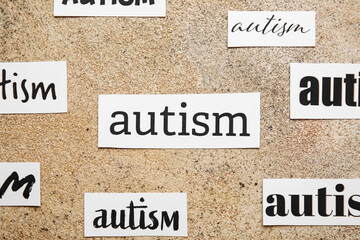 Pieces of paper with words AUTISM on grunge background, closeup