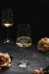 Glass of white wine chardonnay and roses on dark background