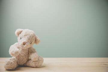 A single brown teddy bear sitting on an old wooden table filling sad, alone with copy space. This...