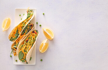 Plate with tasty tacos and lemon on light background