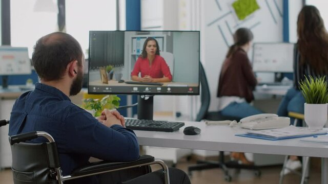 Handicapped manager talking on videocall with team leader sitting in front of camera at computer during virtual conference working in strat up business office. Diverse team planning strategy
