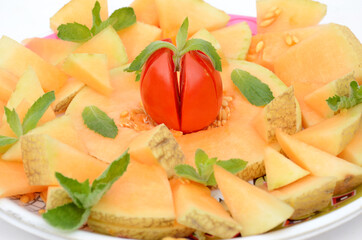 closeup sliced ripe orange muskmelon with red tomato and mint isolated on white background.