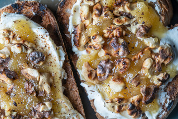 Two bread toast with cream cheese, roasted walnuts, honey, pepper and salt, close up, top view