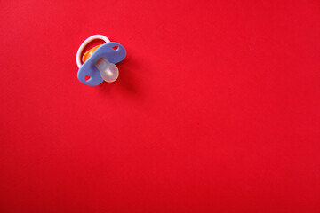 Baby pacifier on a red background, top view, place for an inscription