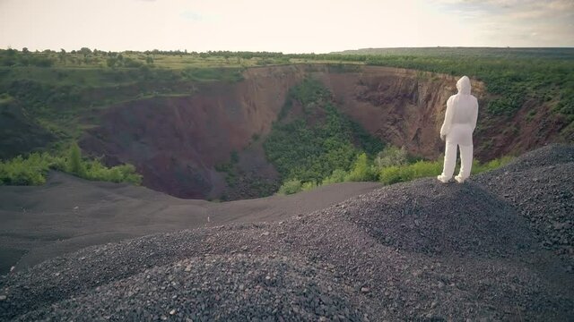 a man in a white bacteriological protective suit looks at a huge hole in the ground. Drone shooting