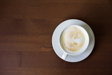 top view of a cup of coffee with milk foam, which stands on the side of a wooden table. copy space.