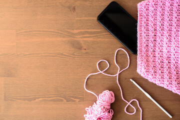 Online courses on learning to crochet. Scarf with a star pattern. Pink thread, a crochet hook and a phone on a wooden background. Copying a space.