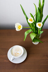 top view of a bouquet of white tulips and a cup of coffee standing on the table.
