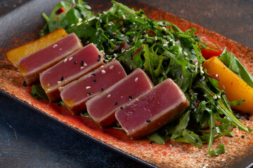 Fried tuna in slices with fresh tomatoes, sesame seeds and arugula salad