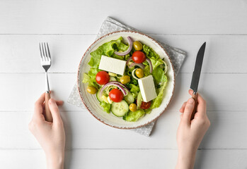 Woman eating fresh salad on light wooden background