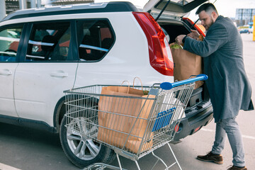 man putting bags with product in car trunk