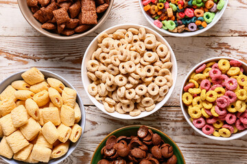 Bowls with different cereals on light wooden background, closeup