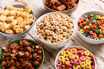 Bowls with different cereals on light wooden background, closeup