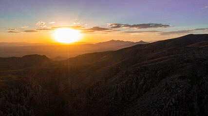 Aerial view of  mountains in Arizona during sunset with silhouettes in the distance and clouds.