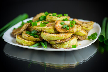 fried zucchini in circles with fresh herbs in a plate on a black