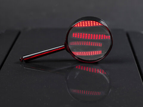 Fototapeta Magnifying glass or zooming lens on dark black background with red light flares. Searching and detective concept.