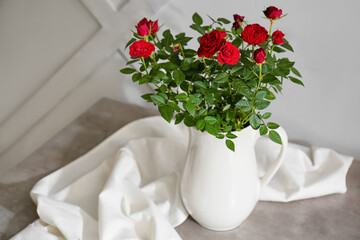 Beautiful red roses in pot on table near light wall