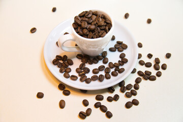 White cup on saucer filled with brown coffee beans on a white background. Confectionery products drinks tea coffee.