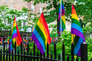 Several Rainbow Pride flags displayed on the metal fence of Christopher Park. Green landscape