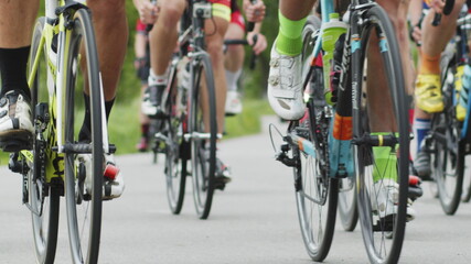 Fototapeta na wymiar Shallow focus shot of cyclists lower bodies while riding bikes in cycling race. The bicycle wheel is spinning. Bicycle wheel rotation. Cyclist training. Sports Healthy lifestyle.
